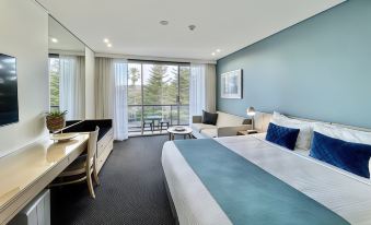 a modern hotel room with a large bed , desk , and balcony , decorated in blue and white colors at Coogee Sands Hotel & Apartments