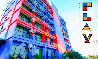 a colorful building with blue and pink stripes on its facade , surrounded by trees and blue skies at Play Phala Beach Rayong