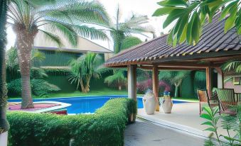 a large swimming pool surrounded by lush greenery , including palm trees and bushes , in front of a house at Coconut Lodge