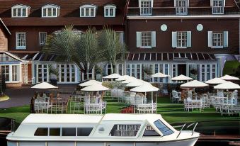 a large white boat docked next to a building with many umbrellas and chairs in front at Macdonald Compleat Angler