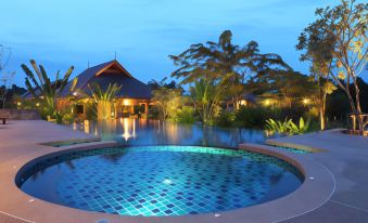 a large , round swimming pool with a blue tiled edge is surrounded by lush greenery and lit up at night at Chalicha Resort