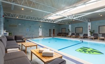 a modern indoor swimming pool area with wooden tables , lounge chairs , and a large indoor pool at The Billesley Manor Hotel