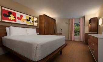 a large bed with white sheets and a wooden headboard is in a room with pink curtains at Disney's Pop Century Resort - Classic Years