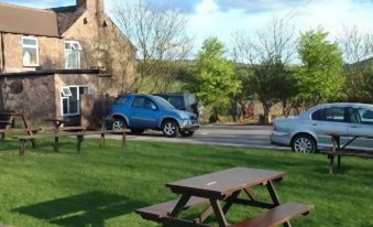 a picnic table and benches in a grassy area near a building , with cars parked nearby at The Stanley Arms