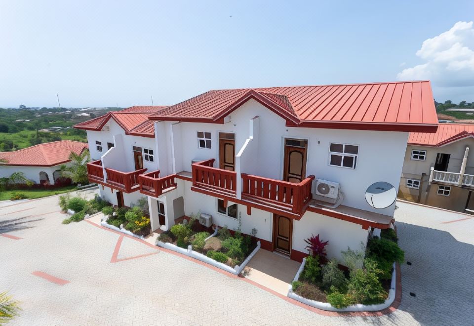 a white and red building with a balcony is surrounded by greenery and has a balcony at Royal Elmount Hotel