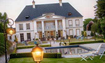 a large white house with a fountain in front of it , surrounded by a grassy field at Hôtel la Ramade