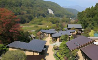 a scenic view of a hillside with houses and trees , surrounded by mountains and a waterfall at Fuefukigawa Onsen Zabou