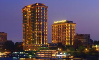 two tall buildings are lit up at night , with a boat on the water in front of them at Four Seasons Hotel Cairo at the First Residence