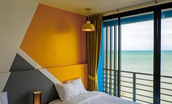 a bedroom with a large window overlooking the ocean , featuring yellow and orange walls , a white bed , and a lamp at Play Phala Beach Rayong