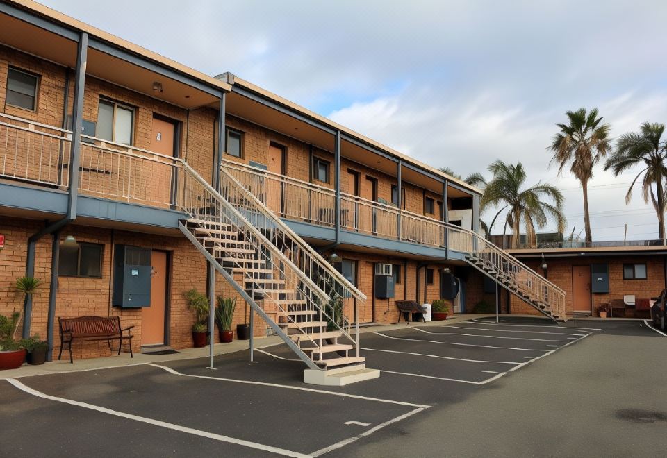 a brick building with a staircase leading to the second floor , surrounded by palm trees and other greenery at Bridge View Motel