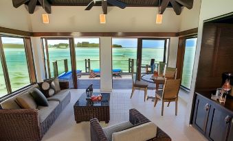 a spacious living room with a couch , chairs , and tables is shown with a view of the ocean at Warwick le Lagon Resort & Spa, Vanuatu