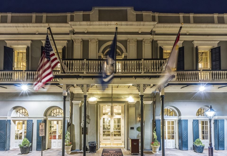 a large building with two flags hanging from the front porch , illuminating the night sky at Bourbon Orleans Hotel
