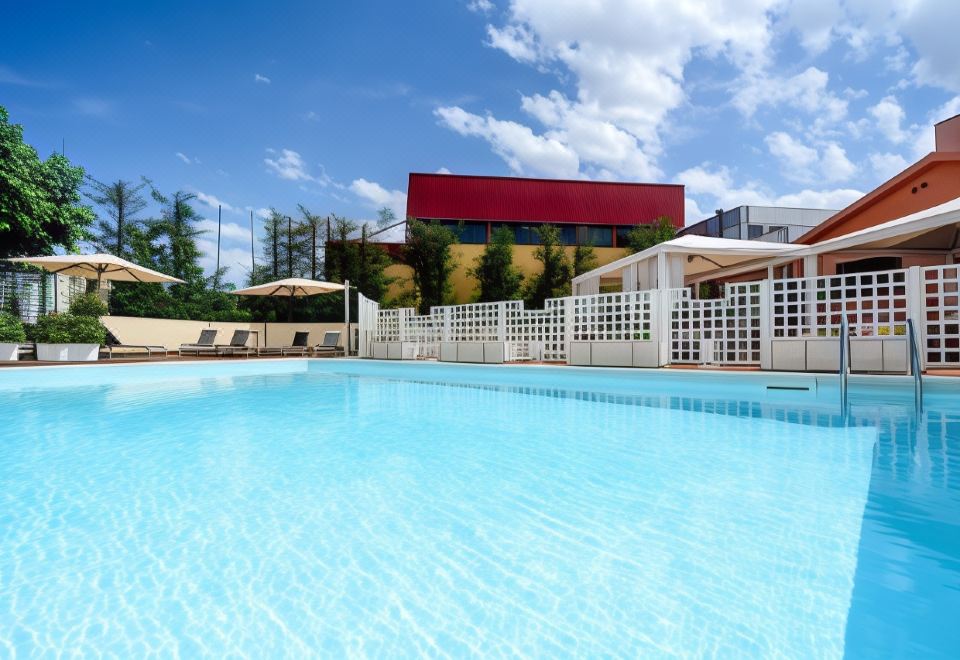 a large swimming pool with a red building in the background and white umbrellas surrounding it at Hotel Concorde