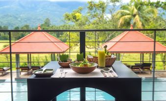 a table with a bowl of fruit and a glass of orange juice is set on an outdoor balcony overlooking mountains at Jetwing Kaduruketha