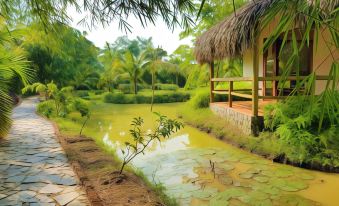 a serene garden with a thatched - roof hut , a pond , and lush greenery surrounding a path at Riverside Park Eco Resort