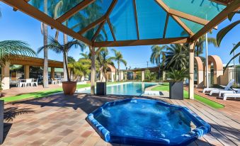 a hot tub is surrounded by a pool and palm trees , with a covered patio area in the background at Ingot Hotel Perth, Ascend Hotel Collection