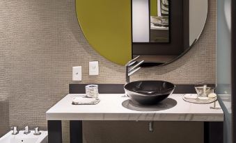 a modern bathroom with a white sink , black bowl , and green accent wall , as well as a large round mirror above the sink at Kos Pilar Hotel