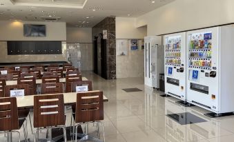 a modern airport terminal with wooden tables and chairs , a vending machine , and multiple signs on the wall at Toyoko Inn Meitetsu Chiryu Ekimae