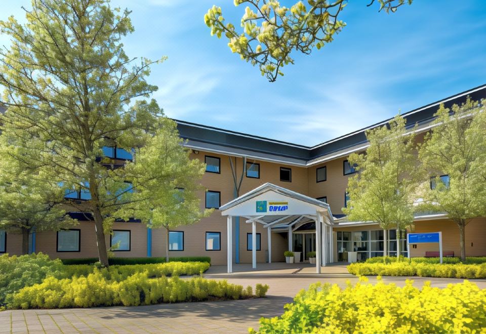 a modern hotel building with a green lawn and trees in front , under a clear blue sky at Holiday Inn Express Milton Keynes