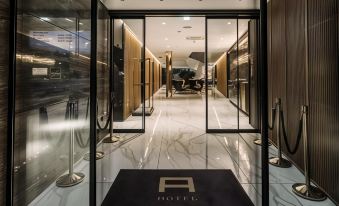"a hotel entrance with a large glass door , gold fixtures , and a black carpet that says "" h ""." at Hotel A