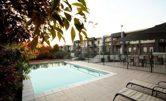 a large swimming pool is surrounded by lounge chairs and trees , with apartment buildings in the background at Quest Ipswich