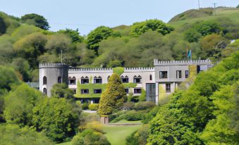 a large , multi - story building with a castle - like design is situated on a hillside surrounded by trees at Abbeyglen Castle Hotel