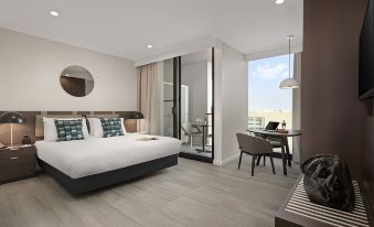 a modern hotel room with a large bed , white walls , and a view of the city through a window at Quest Innaloo