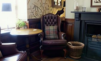 a brown leather armchair with a plaid pillow is sitting next to a wooden table and a fireplace at Black Lion Hotel