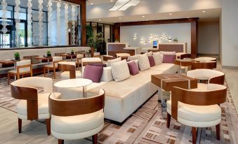 a spacious lounge area with white couches , chairs , and tables , creating a comfortable and inviting atmosphere at Marriott East Lansing at University Place