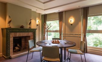 a dining room with a round table surrounded by chairs , and a fireplace in the background at Les Etangs de Corot