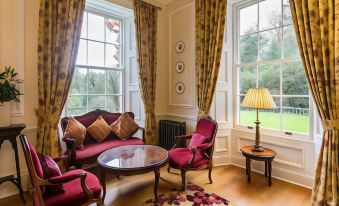 a cozy living room with red furniture , wooden flooring , and large windows overlooking a garden at Doxford Hall Hotel and Spa