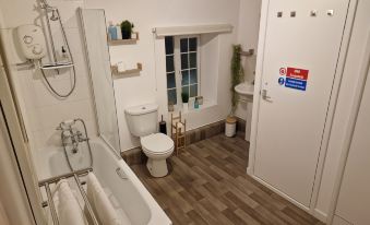 a clean and well - organized bathroom with wooden flooring , white walls , and a bathtub , along with a toilet and sink at The Village Inn