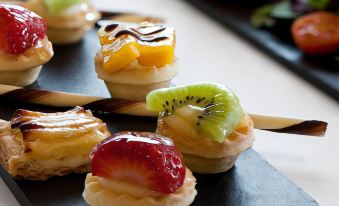 a dining table with a variety of desserts , including fruit tarts and cupcakes , placed on a black slate plate at Hesperia Barcelona Sant Just