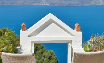 a balcony with two wicker chairs , a table , and a view of the ocean and mountains in the distance at Belvedere Suites