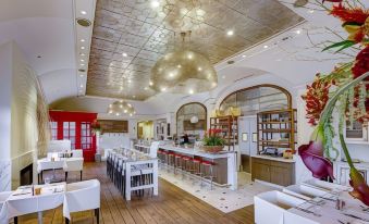 a modern restaurant with a bar area , white chairs , and a wooden floor , surrounded by large windows at The H Hotel