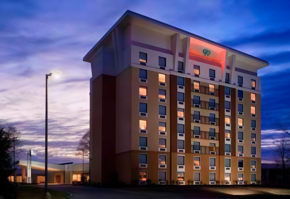 a large hotel building with a red sign on the front is lit up at night at DoubleTree by Hilton Hotel Cincinnati Airport