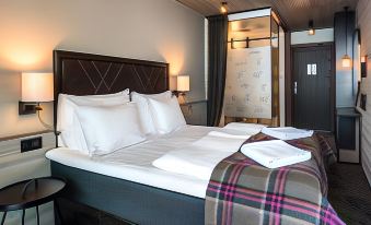 a bed with white sheets and a plaid blanket is shown in a hotel room at Langley Hotel Tignes 2100