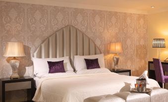 a large bed with white linens and purple pillows is situated in a room with beige walls at Castle Hotel Macroom