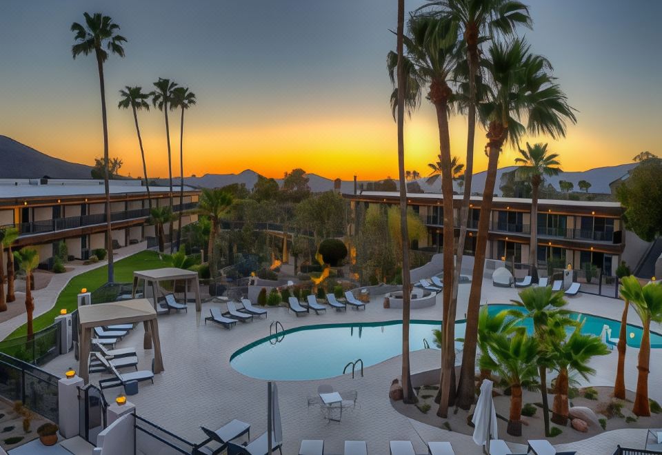 a large pool is surrounded by lounge chairs and palm trees , with the sun setting in the background at Civana Wellness Resort & Spa