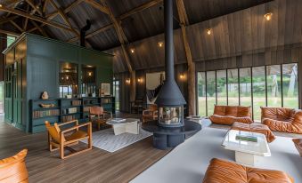 a modern living room with a large fire pit , leather chairs , and wooden floors , surrounded by windows at Les Sources de Cheverny