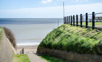 a grassy hillside next to a beach , with a fence and stairs leading down to the water at The Ship Inn