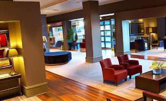 a modern hotel lobby with wooden floors , red chairs , and large windows , as well as a blue couch and coffee table at Village Hotel Birmingham Dudley