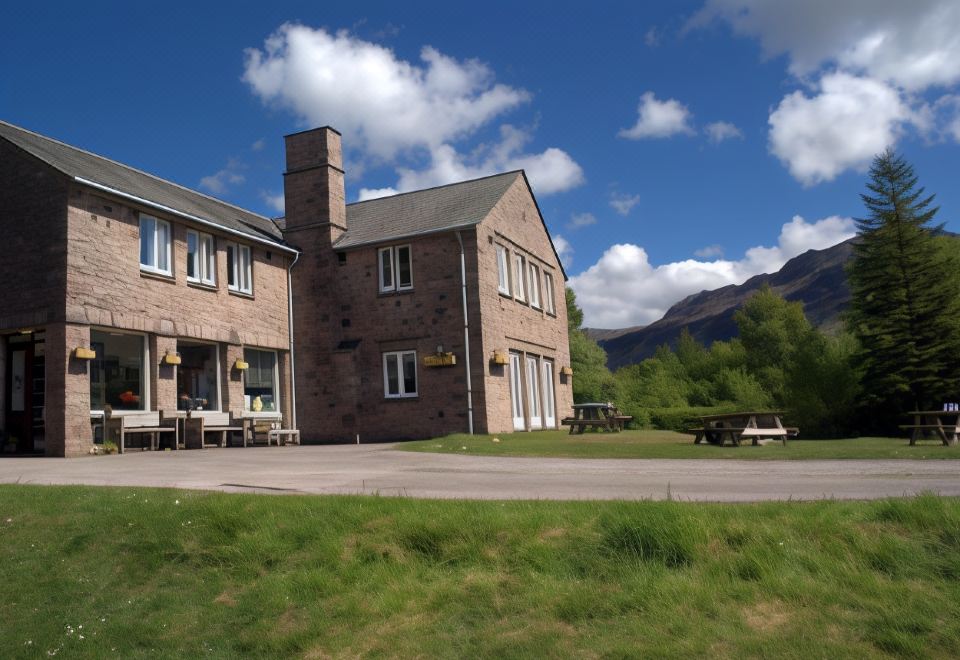 a brick house with a chimney and a grassy field in front of it , under a cloudy blue sky at YHA Eskdale