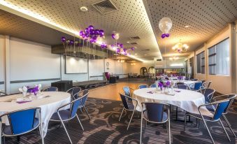 a large banquet hall filled with tables and chairs , decorated with purple balloons and flowers at Nightcap at Skyways Hotel