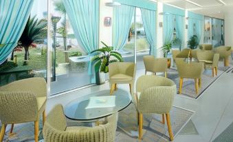 a modern hotel lobby with comfortable seating , dining areas , and large windows offering views of the ocean at Hotel Miramare