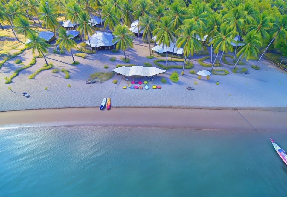 aerial view of a sandy beach with several boats docked , surrounded by palm trees and buildings at Coconut Garden Beach Resort