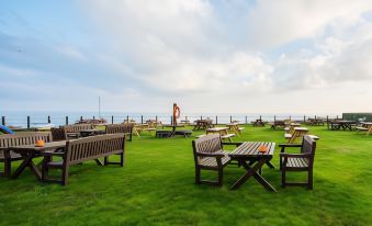 a grassy area with wooden benches and tables , overlooking the ocean , under a partly cloudy sky at The Ship Inn