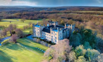 aerial view of a large castle surrounded by green fields and trees , with a golf course in the foreground at Lumley Castle Hotel