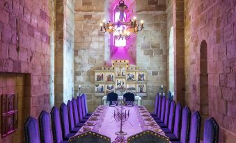 a long dining table is set in a stone room with purple lights and a chandelier at Parador de Siguenza
