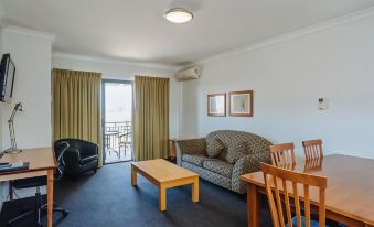 a living room with a couch , chairs , and dining table is shown with a view of the balcony at Canning Bridge Auto Lodge